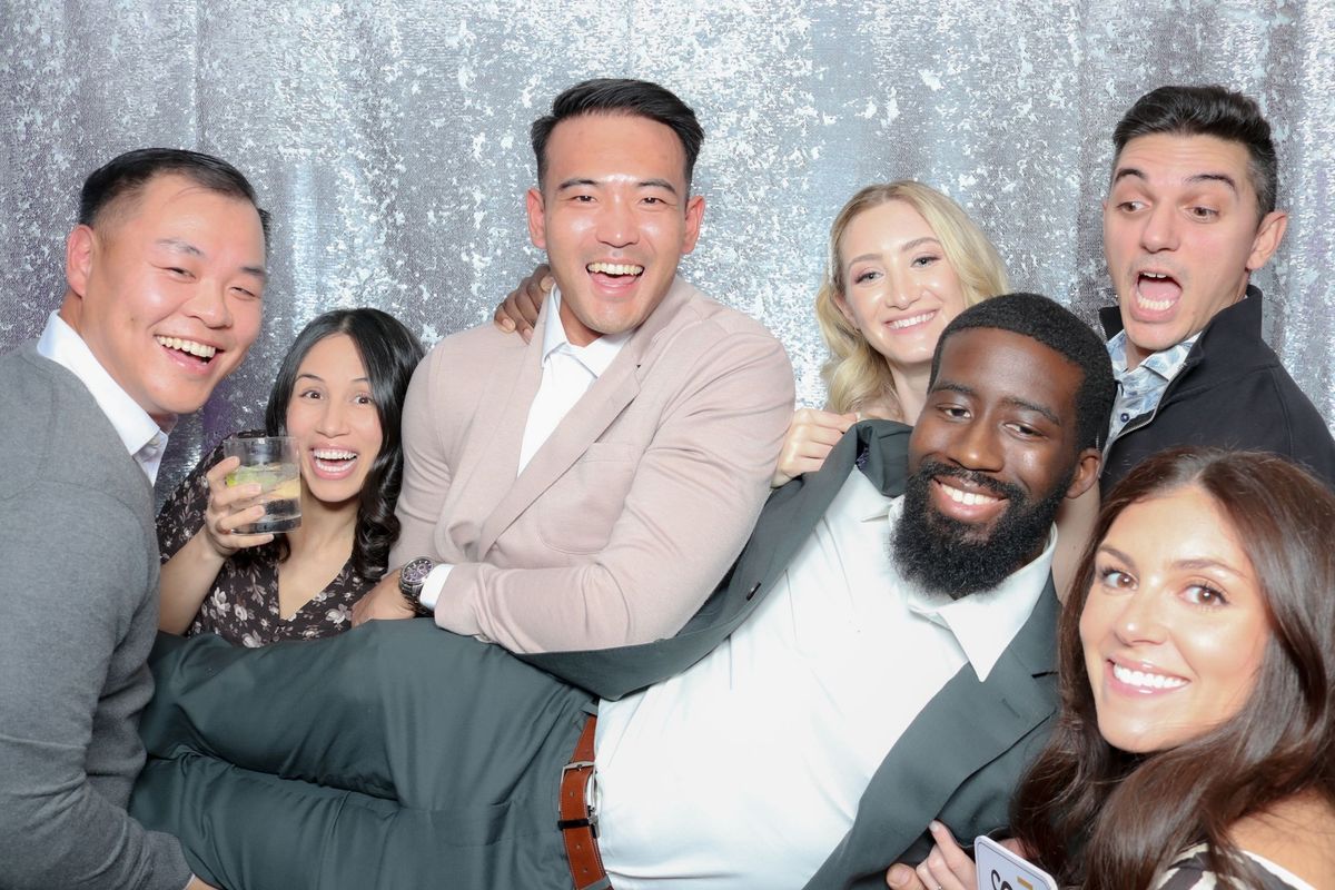 Laughing colleagues carrying a coworker across their arms in front of a silver sequin backdrop