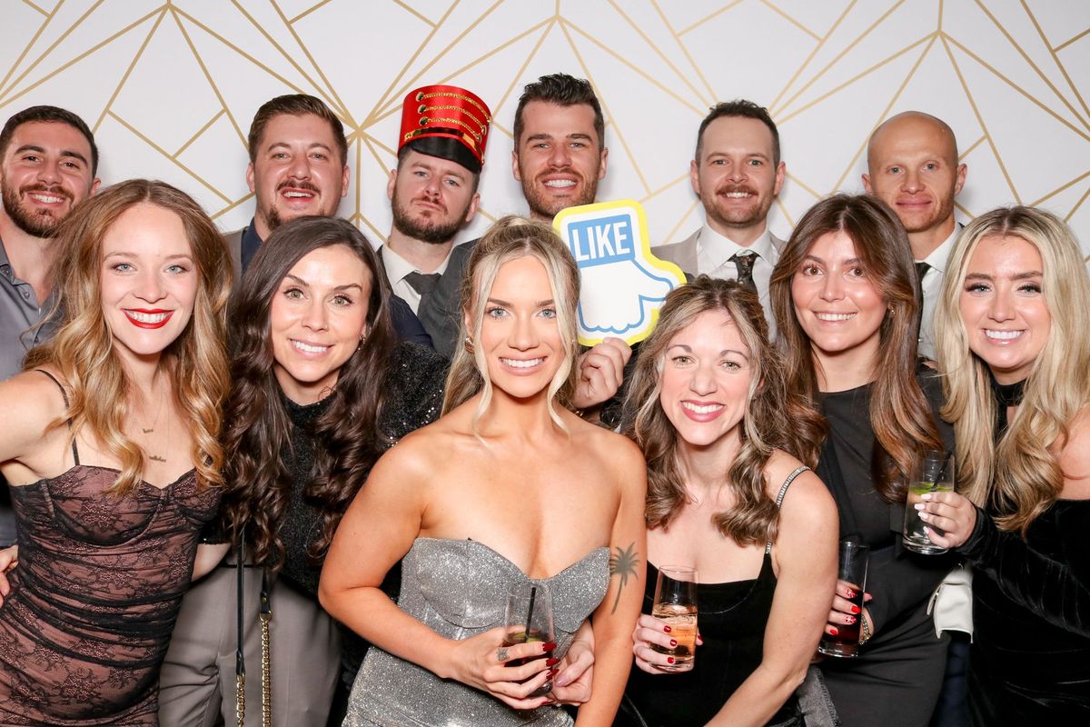 Eleven colleagues dressed up for an evening event, posing in front of a gold geometric backdrop with a “Like” sign