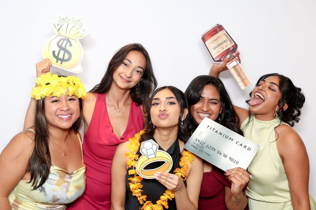 Five friends at a party posing with a money bag, a giant ring and a credit card prop