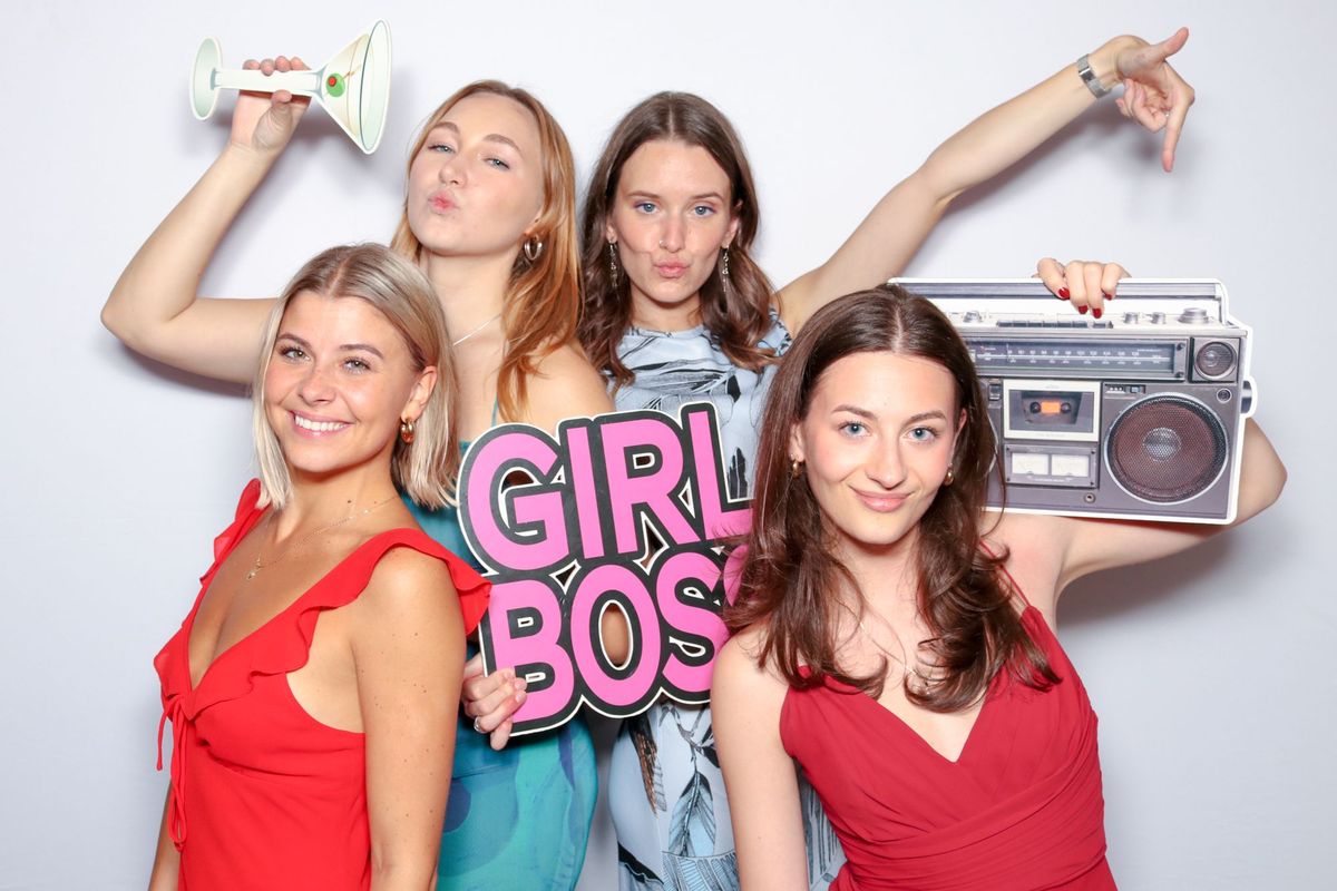 Four friends posing with a pink “Girl Boss” sign, a boombox and a cocktail glass prop in front of a white backdrop