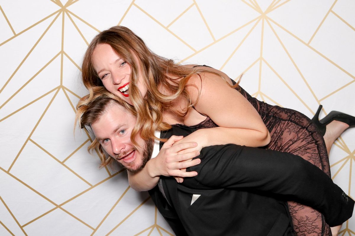 A laughing couple doing a piggyback ride in front of a gold geometric backdrop