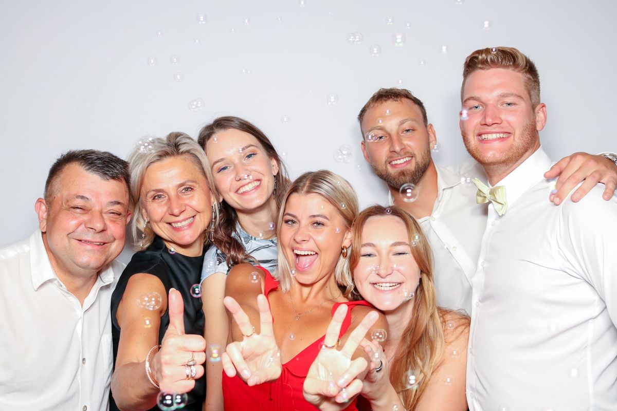 A family group at a wedding making peace signs and thumbs up as bubbles float around them
