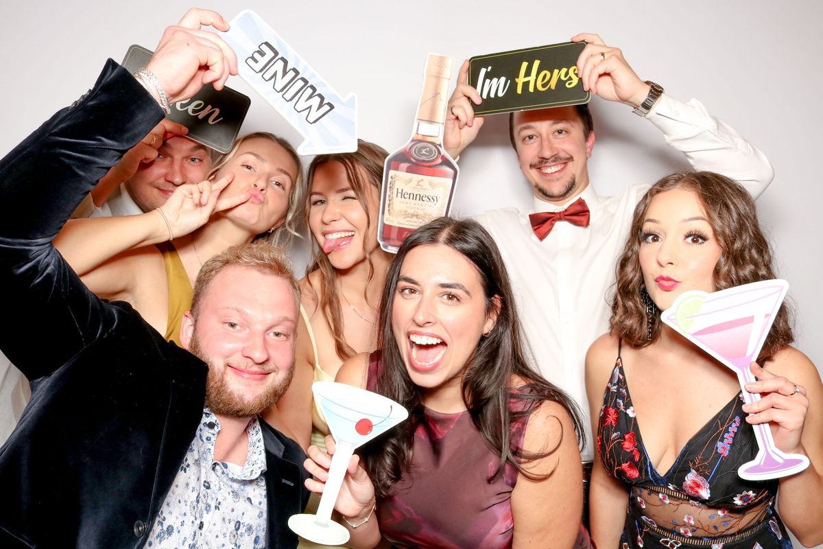 A big group of wedding guests holding cocktail, “Mine” and “I’m Hers” sign props